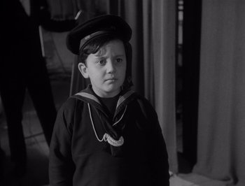 Movie still from “I Vitelloni” (1953), directed by Federico Fellini – A young boy wearing a sailor suit and a hat; Close Up shot, High angle