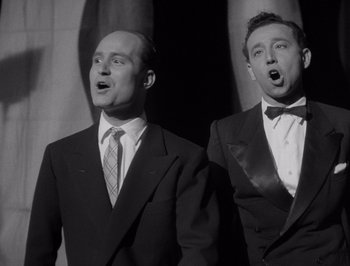 Movie still from “I Vitelloni” (1953), directed by Federico Fellini – A couple of men standing next to each other; Medium shot, Low angle