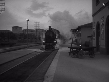 Movie still from “I Vitelloni” (1953), directed by Federico Fellini – A train is coming down the tracks at a station; Extreme Wide shot, High angle