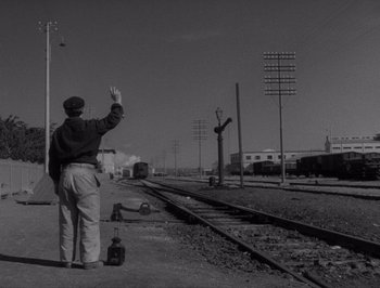 Movie still from “I Vitelloni” (1953), directed by Federico Fellini – A man standing on the side of a train track waving; Wide shot, Low angle