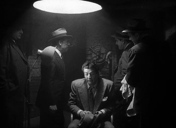 Movie still from “I Wake Up Screaming” (1941), directed by H. Bruce Humberstone – A group of men standing around a man in a suit and tie; Medium shot, Low angle
