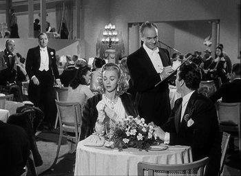Movie still from “I Wake Up Screaming” (1941), directed by H. Bruce Humberstone – A woman sitting at a table with a man in a tuxedo; Medium shot, Over the shoulder angle