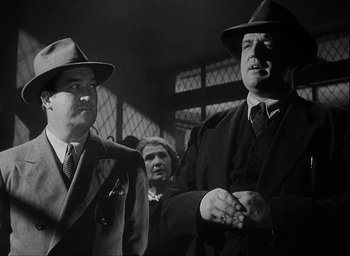Movie still from “I Wake Up Screaming” (1941), directed by H. Bruce Humberstone – A man in a suit and a man in a hat; Medium shot, Low angle