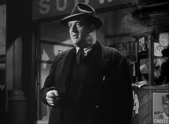 Movie still from “I Wake Up Screaming” (1941), directed by H. Bruce Humberstone – A man in a suit and a hat is smoking a cigarette; Medium shot, Low angle