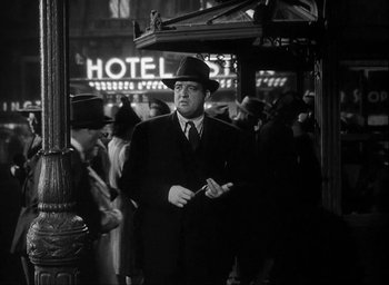 Movie still from “I Wake Up Screaming” (1941), directed by H. Bruce Humberstone – A black and white photo of a man in a suit and hat; Medium shot, Low angle