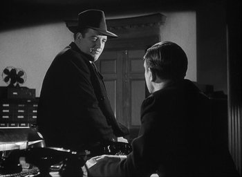 Movie still from “I Wake Up Screaming” (1941), directed by H. Bruce Humberstone – A man wearing a hat talking to another man in front of a chair; Medium shot, Over the shoulder angle