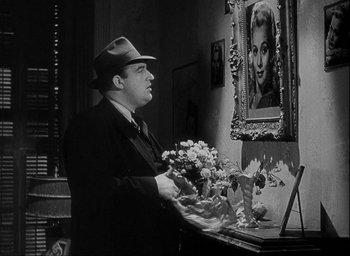 Movie still from “I Wake Up Screaming” (1941), directed by H. Bruce Humberstone – A black and white photo of a man holding a bouquet of flowers in front of a portrait of a woman; Medium shot, Over the shoulder angle