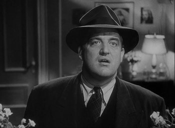 Movie still from “I Wake Up Screaming” (1941), directed by H. Bruce Humberstone – A man wearing a suit and a hat in a black and white photo; Close Up shot, Low angle