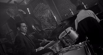 Movie still from “I Want to Live!” (1958), directed by Robert Wise – A man playing drums in front of another man; Medium shot, Over the shoulder angle