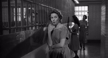 Movie still from “I Want to Live!” (1958), directed by Robert Wise – An old black and white photo of a woman standing in front of a fence; Medium shot, Over the shoulder angle