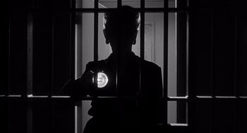 Movie still from “I Want to Live!” (1958), directed by Robert Wise – A person holding a cell phone in a jail cell; Medium shot, Low angle
