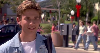 Movie still from “I'll Be Home for Christmas” (1998), directed by Arlene Sanford – A young man with a backpack smiles for the camera; Close Up shot, Over the shoulder angle