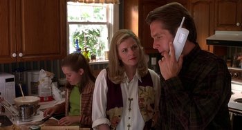 Movie still from “I'll Be Home for Christmas” (1998), directed by Arlene Sanford – A man talking on a phone while a woman and a little girl look on; Close Up shot, Over the shoulder angle
