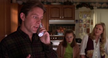 Movie still from “I'll Be Home for Christmas” (1998), directed by Arlene Sanford – A man talking on a cell phone in front of a woman; Close Up shot, Over the shoulder angle