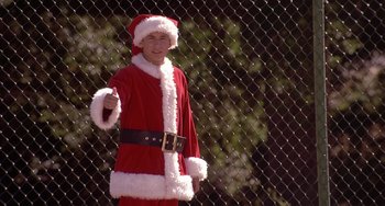 Movie still from “I'll Be Home for Christmas” (1998), directed by Arlene Sanford – A man dressed up as santa claus standing in front of a fence; Medium shot, Low angle