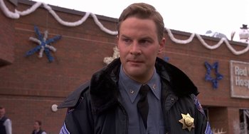 Movie still from “I'll Be Home for Christmas” (1998), directed by Arlene Sanford – A man in a police uniform standing in front of a brick building; Close Up shot, Low angle