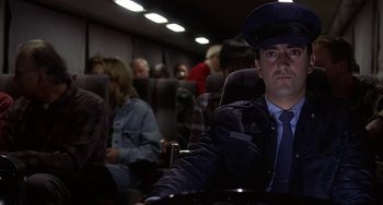 Movie still from “I'll Be Home for Christmas” (1998), directed by Arlene Sanford – A man sitting in an airplane seat wearing a hat; Medium shot, Low angle