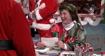 Movie still from “I'll Be Home for Christmas” (1998), directed by Arlene Sanford – A woman dressed as a christmas elf smiles while holding an envelope; Close Up shot, Over the shoulder angle