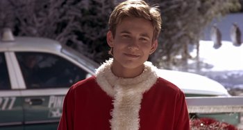 Movie still from “I'll Be Home for Christmas” (1998), directed by Arlene Sanford – A boy in a santa clause outfit standing in front of a tree; Close Up shot, Over the shoulder angle