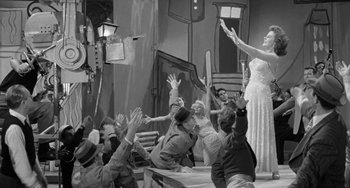 Movie still from “I'll Cry Tomorrow” (1955), directed by Daniel Mann – A group of people sitting on a stage with a woman in a dress; Wide shot, High angle