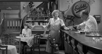 Movie still from “I'll Cry Tomorrow” (1955), directed by Daniel Mann – A woman standing at a counter in front of a counter; Wide shot, Low angle