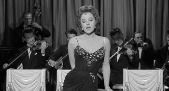 Movie still from “I'll Cry Tomorrow” (1955), directed by Daniel Mann – A woman in a black dress is standing in front of a group of people; Medium shot, Low angle