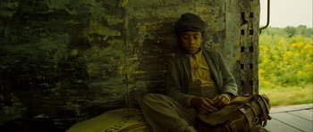 Movie still from “I'm Not There” (2007), directed by Todd Haynes – A young man sitting on a pillow in a room; Medium shot, High angle