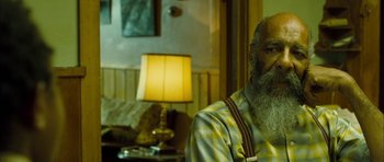 Movie still from “I'm Not There” (2007), directed by Todd Haynes – An older man with a long beard sitting next to a lamp; Close Up shot, Over the shoulder angle