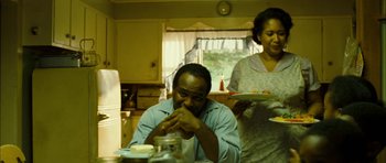 Movie still from “I'm Not There” (2007), directed by Todd Haynes – A man sitting at a table with a plate in front of him; Medium shot, Over the shoulder angle