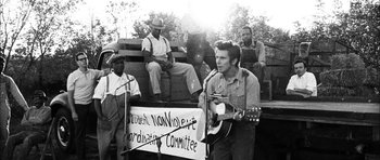 Movie still from “I'm Not There” (2007), directed by Todd Haynes – A man is playing a guitar in front of a group of people; Medium shot, Low angle