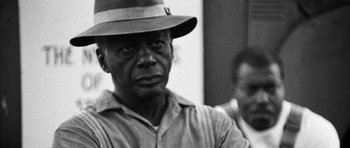 Movie still from “I'm Not There” (2007), directed by Todd Haynes – An older man wearing a hat and looking at the camera; Close Up shot, Over the shoulder angle