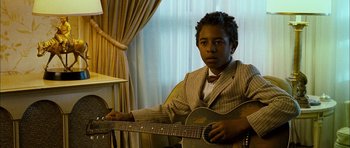 Movie still from “I'm Not There” (2007), directed by Todd Haynes – A young man holding a guitar while sitting in a chair; Close Up shot, Over the shoulder angle