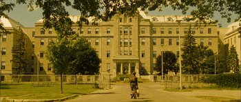 Movie still from “I'm Not There” (2007), directed by Todd Haynes – A person riding a bike down a street near a building; Extreme Wide shot, High angle