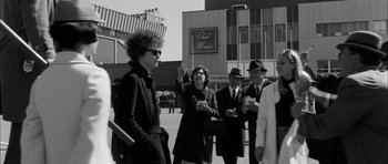 Movie still from “I'm Not There” (2007), directed by Todd Haynes – A black and white photo of a group of people standing around; Medium shot, Over the shoulder angle