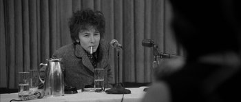Movie still from “I'm Not There” (2007), directed by Todd Haynes – A person sitting at a table with a microphone; Medium shot, Over the shoulder angle