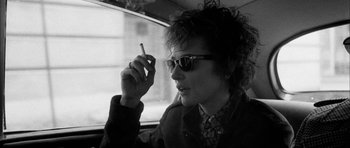 Movie still from “I'm Not There” (2007), directed by Todd Haynes – A man in sunglasses smoking a cigarette while sitting in a car; Close Up shot, Low angle