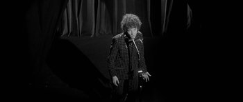 Movie still from “I'm Not There” (2007), directed by Todd Haynes – A man standing in front of a curtain on a stage; Medium shot, High angle