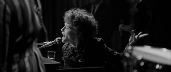 Movie still from “I'm Not There” (2007), directed by Todd Haynes – A man with curly hair is singing into a microphone; Medium shot, Low angle