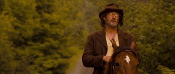 Movie still from “I'm Not There” (2007), directed by Todd Haynes – A man in a hat and glasses standing next to a horse; Medium shot, Low angle