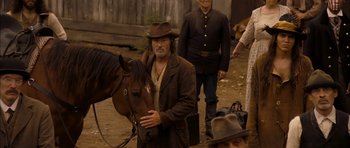 Movie still from “I'm Not There” (2007), directed by Todd Haynes – A man in a brown jacket and a brown hat is holding a brown horse; Medium shot, Over the shoulder angle