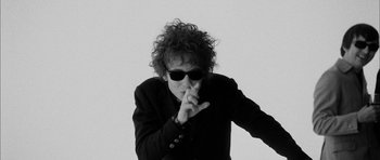 Movie still from “I'm Not There” (2007), directed by Todd Haynes – A black and white photo of a man in a suit and sunglasses; Medium shot, Low angle