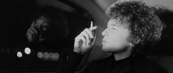 Movie still from “I'm Not There” (2007), directed by Todd Haynes – A man sitting in a car smoking a cigarette; Close Up shot, Over the shoulder angle