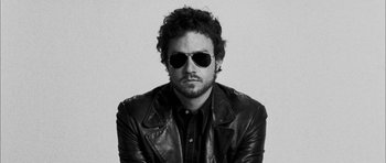 Movie still from “I'm Not There” (2007), directed by Todd Haynes – Black and white photograph of a man wearing sunglasses and a leather jacket; Close Up shot, Low angle