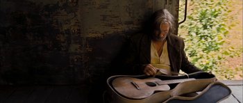 Movie still from “I'm Not There” (2007), directed by Todd Haynes – An older man sitting next to a guitar; Medium shot, Low angle