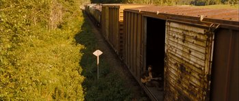 Movie still from “I'm Not There” (2007), directed by Todd Haynes – A man sitting on the side of a train tracks next to train cars; Wide shot, High angle