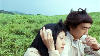 Movie still from “I'm a Cyborg, But That's OK” (2006), directed by Park Chan-wook – Two people sitting in a field with one holding a cell phone to his ear; Medium shot, Low angle