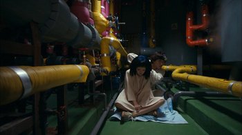 Movie still from “I'm a Cyborg, But That's OK” (2006), directed by Park Chan-wook – A woman sitting on the ground next to pipes; Wide shot, Overhead angle
