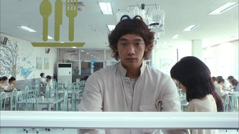 Movie still from “I'm a Cyborg, But That's OK” (2006), directed by Park Chan-wook – A man sitting in front of a bunch of chairs; Close Up shot, Over the shoulder angle