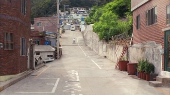 Movie still from “I'm a Cyborg, But That's OK” (2006), directed by Park Chan-wook – A person riding a bike down the middle of a street; Extreme Wide shot, High angle