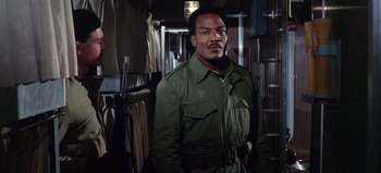 Movie still from “Ice Station Zebra” (1968), directed by John Sturges – A man in a green jacket standing in a room; Medium shot, Low angle